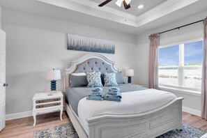 A bedroom with a large bed, two bedside tables, a ceiling fan, and a window with curtains.