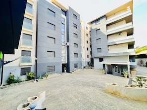A modern residential building with a paved courtyard, multiple balconies, and potted plants.