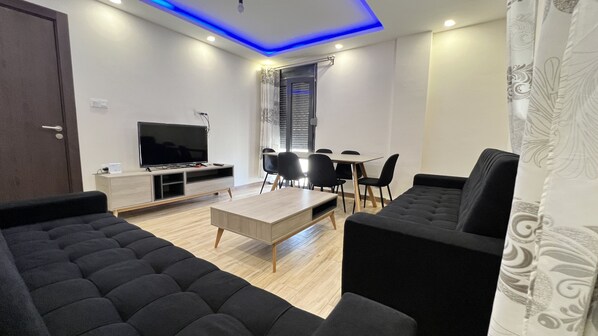 A modern living room with a flat-screen TV, a coffee table, and black sofas.