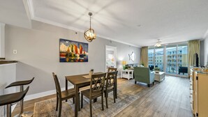 A modern living room with a dining area, a painting on the wall, and a view through large windows. - EscapetoWaterscape-Family Friendly 2/2.5 condo (Fort Walton Beach)