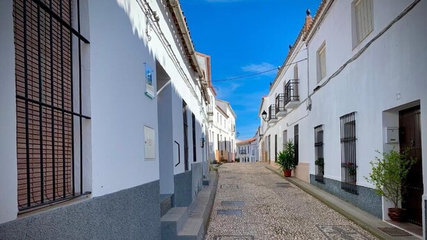 Una estrecha calle adoquinada flanqueada por edificios blancos con rejas y balcones.