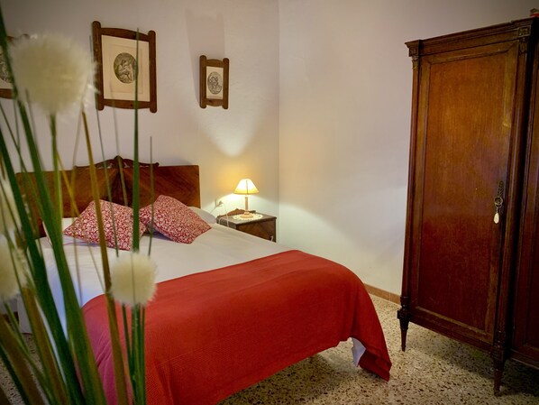 A bedroom with a bed, a nightstand with a lamp, a wooden wardrobe, and two framed pictures on the wall. - Casa Rural Sierra Tórtola 1 (Hinojales)