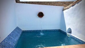 Una pequeña piscina con azulejos azules, un ventanal circular y techo de tejas.