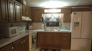 A kitchen with wooden cabinets, a microwave, an oven, a sink, and a refrigerator. - Der Dawdy Haus (Narvon)