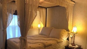 A four-poster canopy bed with a quilted bedspread, two bedside lamps, and a nightstand with a lamp. - Der Dawdy Haus (Narvon)