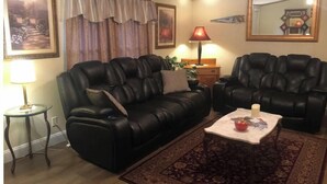 A living room with a black leather sofa set, a small round table, a red lamp, and a patterned rug. - Der Dawdy Haus (Narvon)