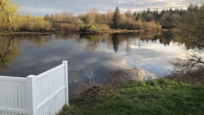 Une vue paisible sur un lac, avec une clôture blanche au premier plan, entourée d’arbres et sous un ciel dégagé.