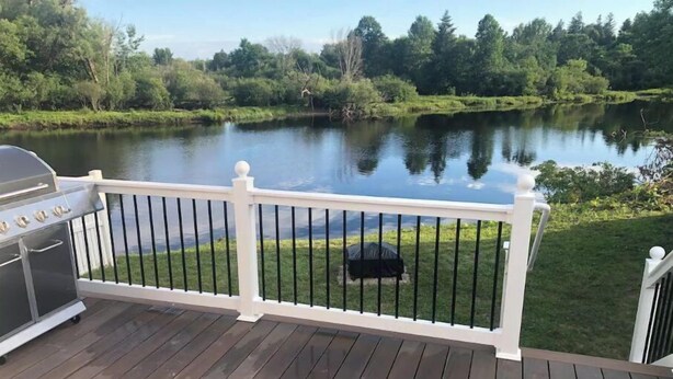 Une terrasse avec un barbecue et vue sur un lac.
