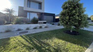 Una moderna casa a due piani con garage, un prato curato e un piccolo albero nel giardino anteriore.