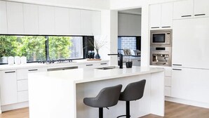 Una cucina moderna con mobili bianchi, un'isola centrale con due sgabelli da bar e vista sul verde circostante.