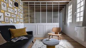 A cozy living room with a black sofa, mustard cushions, a round coffee table, and a wall adorned with framed bird and plant illustrations.