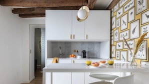 A modern kitchen with white cabinets, a marble backsplash, and a wall of framed botanical illustrations.