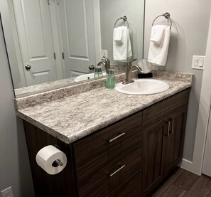 A bathroom with a marble countertop, a white sink, and a wooden vanity with drawers.