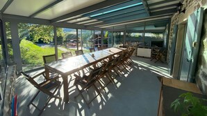 Un comedor moderno con una mesa grande y sillas, ventanas amplias que dan a un jardín y una pared de piedra.