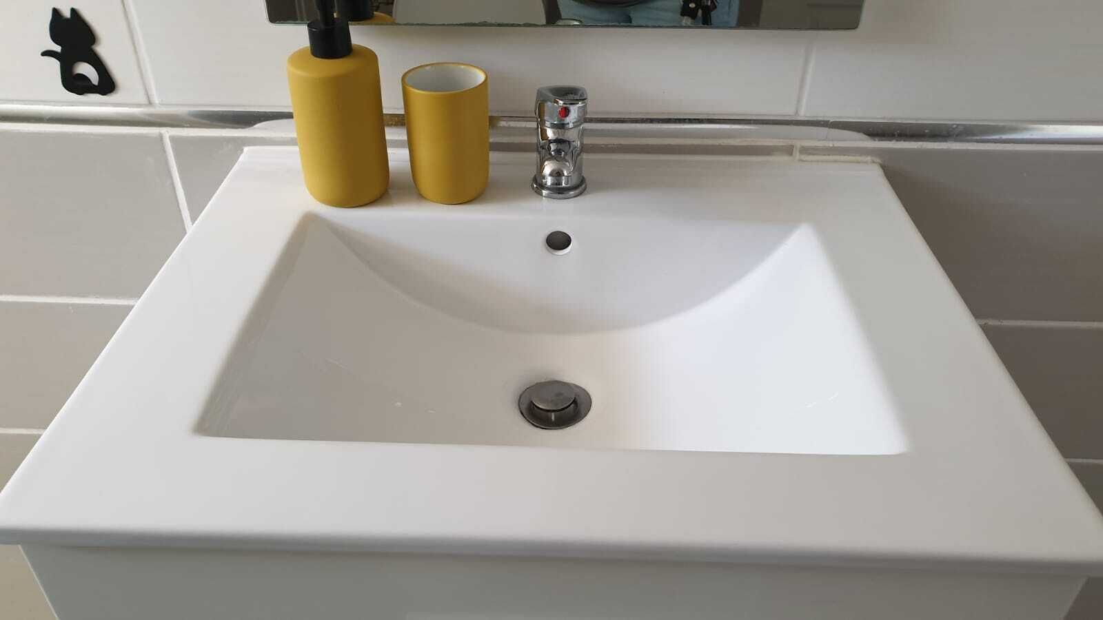 Een witte wastafel met twee gele flessen en een kraan.