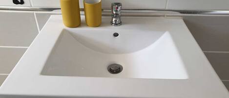 Een witte wastafel met twee gele flessen en een kraan.