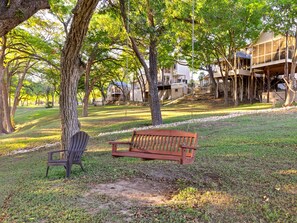 A park with a wooden bench and a chair, surrounded by trees and a building with a sloped roof. - Meyer Hotel (Comfort)