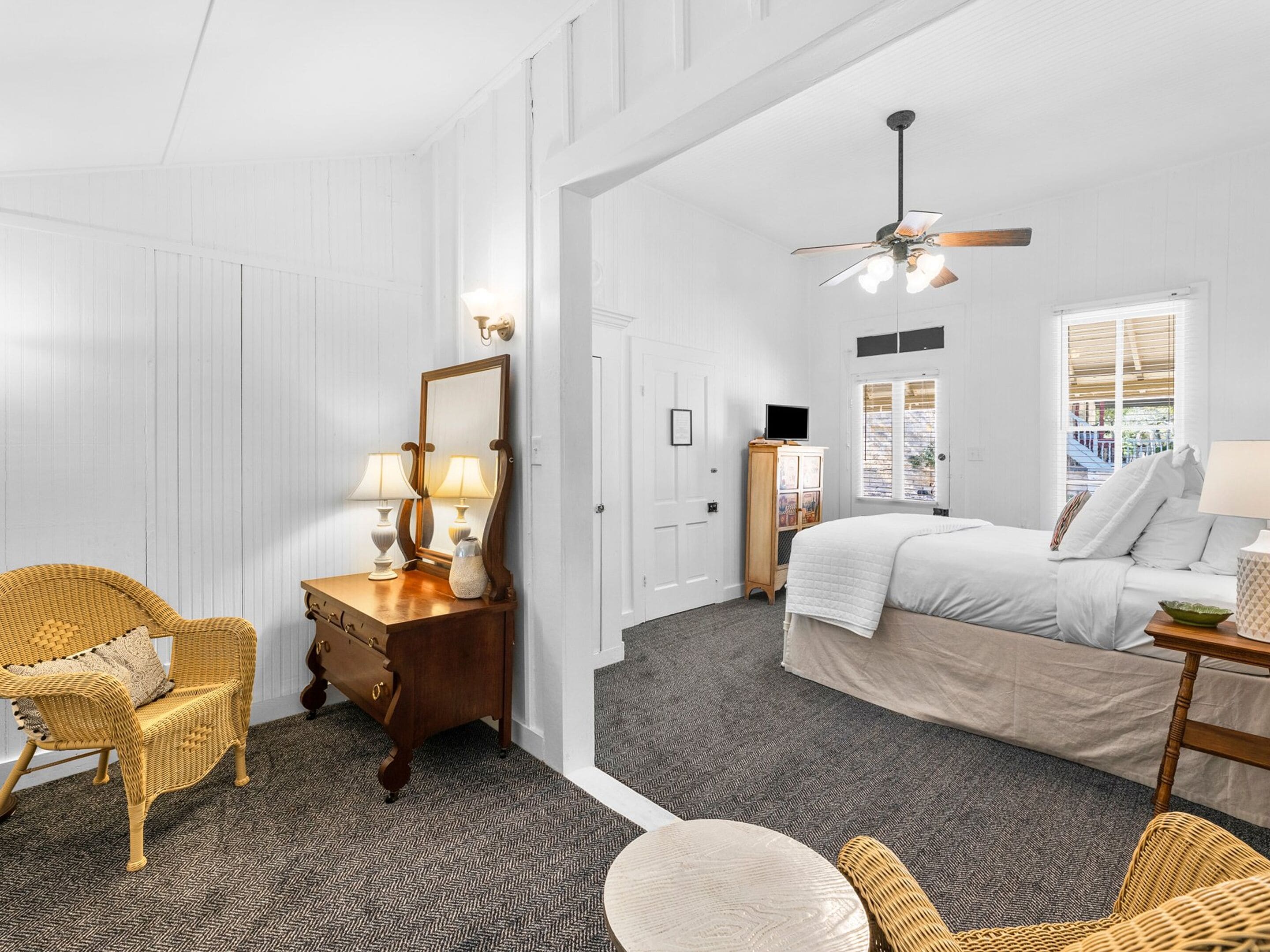 A bedroom with a bed, a chair, a dresser, a mirror, and a ceiling fan.