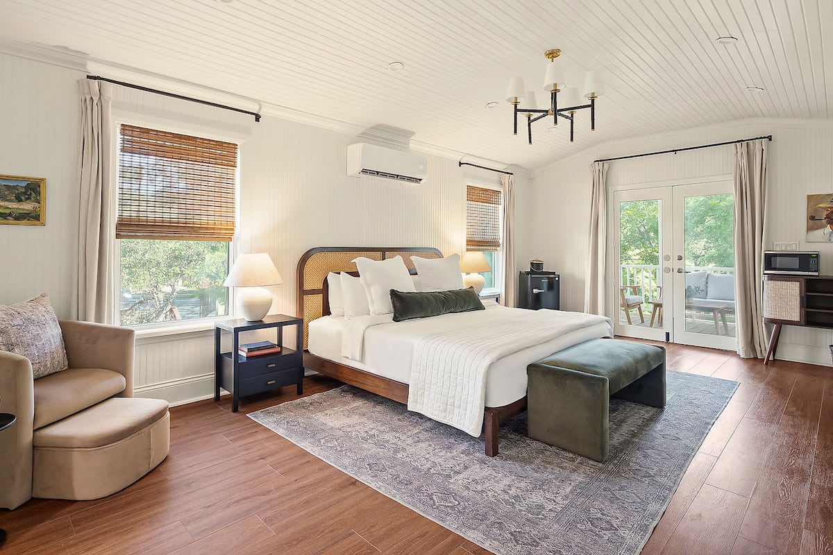 A bedroom with a large bed, bedside tables, a chair, a bench, and a view of the outdoors through a door.