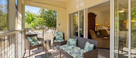 A covered outdoor seating area with wicker furniture and a glass door leading to a patio.
