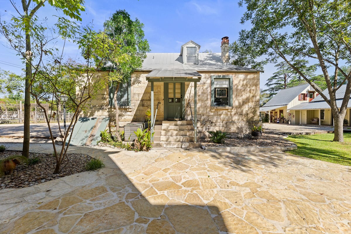 A stone-paved driveway leading to a stone house with a gabled roof, a small porch, and a chimney.