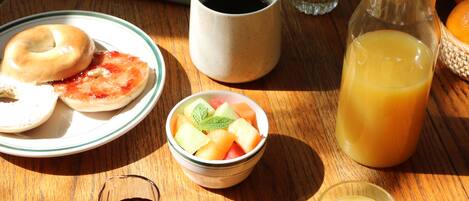 A breakfast setting with a plate of bagels, a bowl of fruit, a cup of coffee, a glass of orange juice, and a pitcher of juice on a wooden table.
