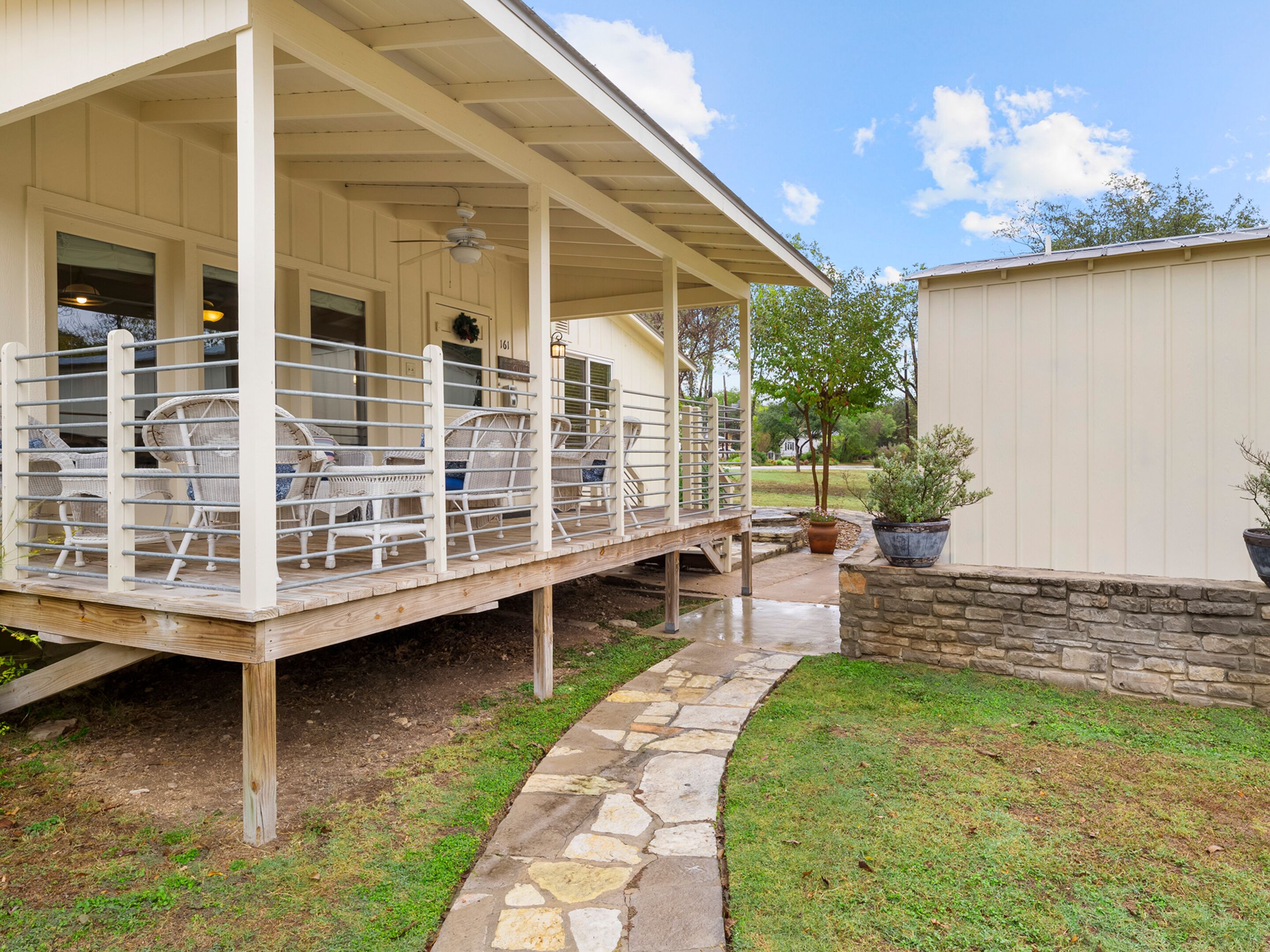 A covered outdoor area with wicker furniture and a stone pathway leading to a house.