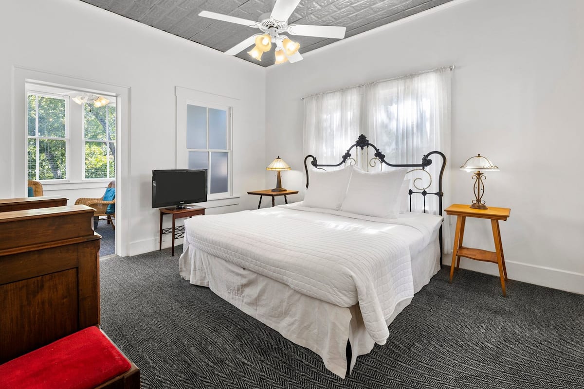 A bedroom with a bed, a television, two bedside tables, and a ceiling fan.