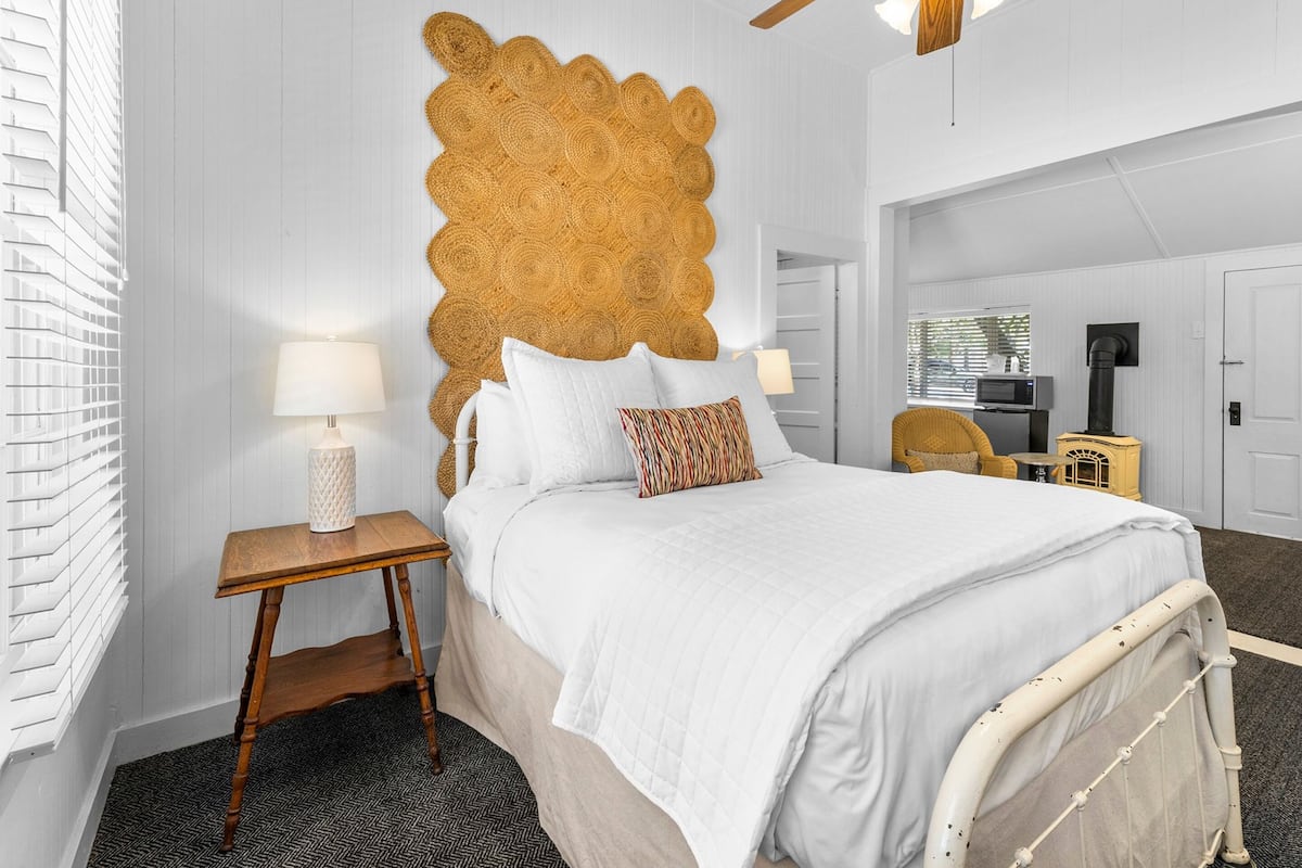 A bedroom with a large bed, a wooden nightstand, a ceiling fan, and a wall-mounted television.