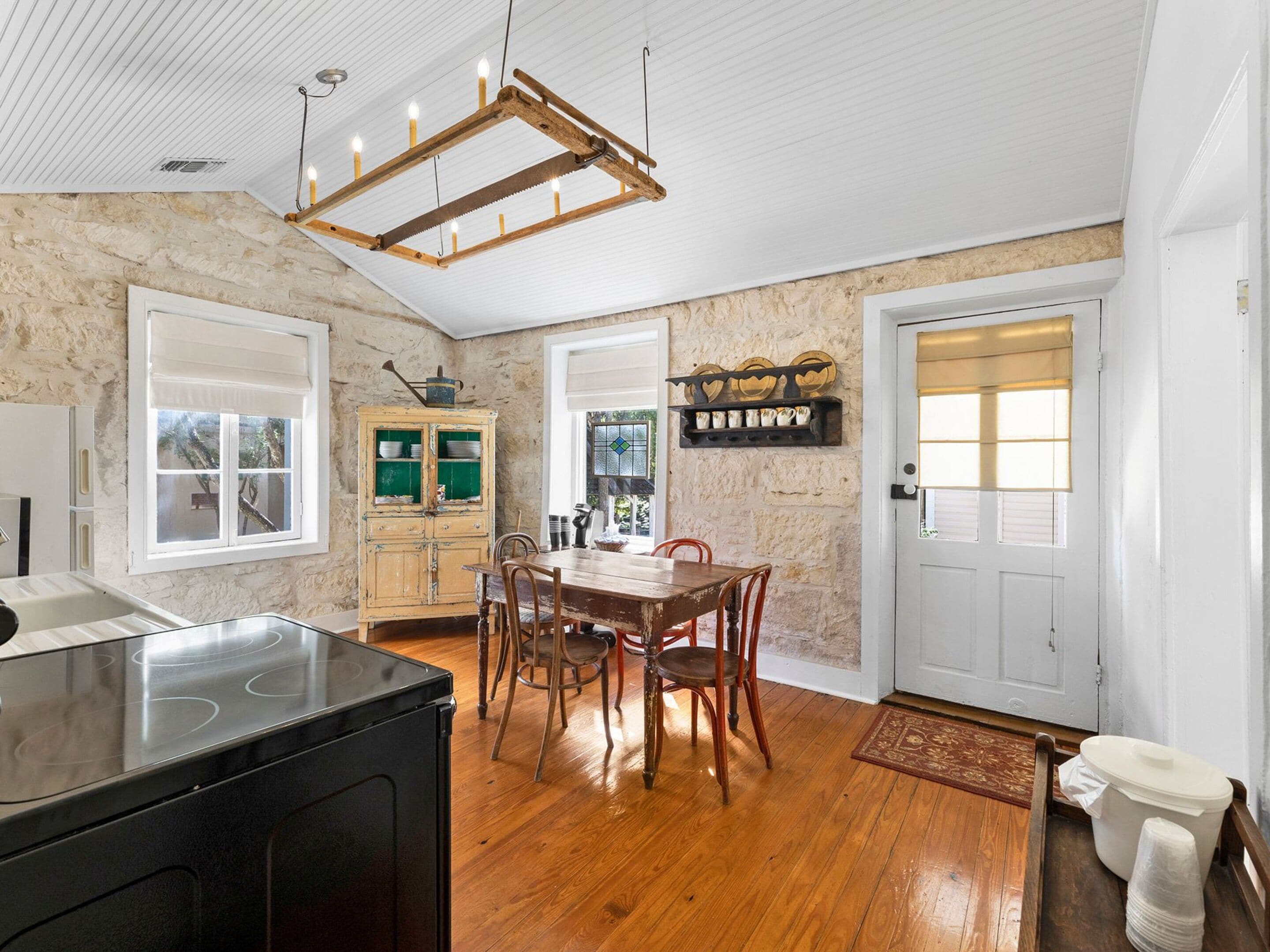 A kitchen with a wooden table, chairs, a stove, and a stone wall.