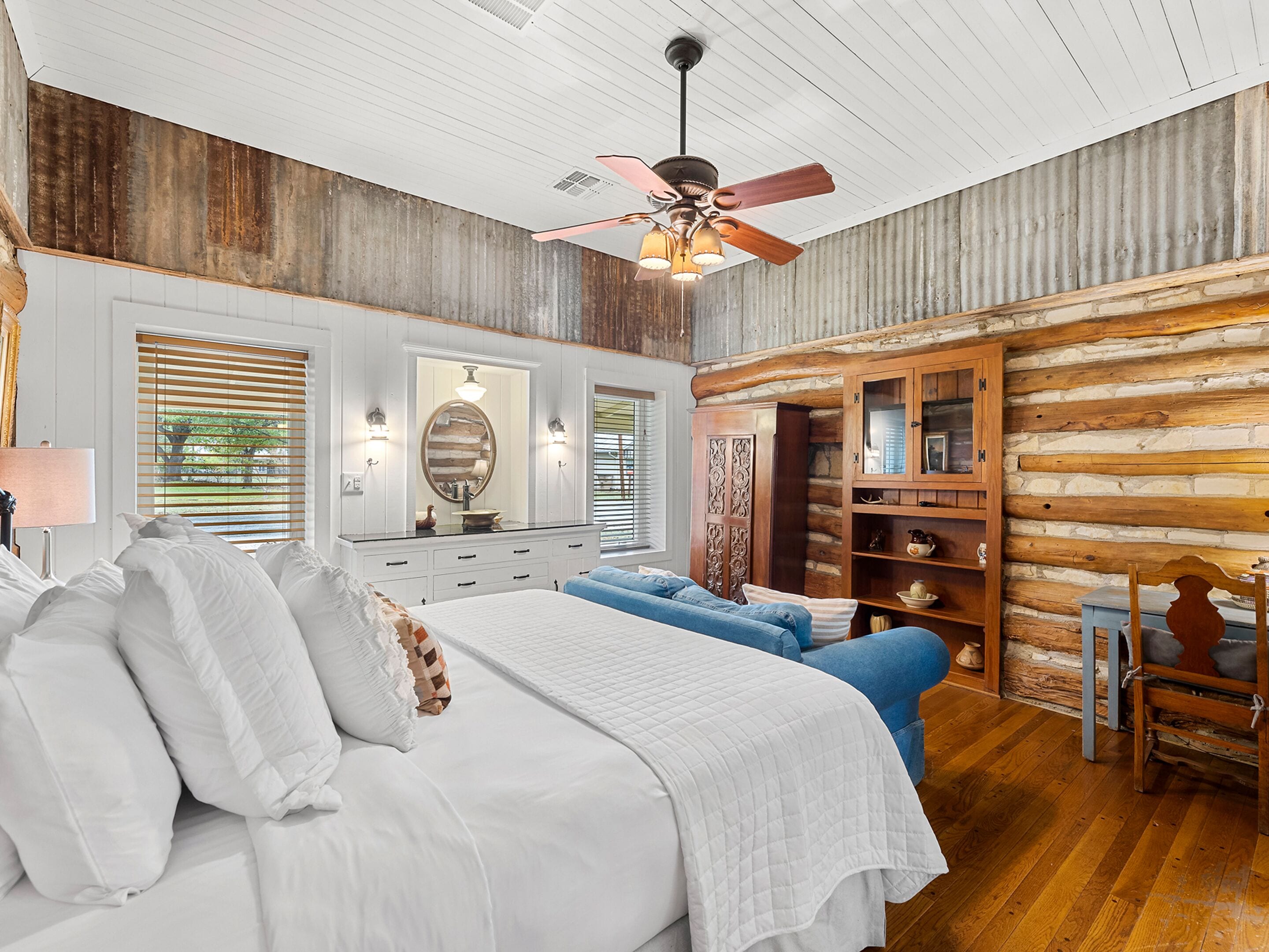 A bedroom with a bed, dresser, vanity, and a wooden cabinet.