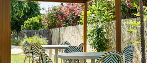 Un patio exterior con sillas de mimbre y una mesa, rodeado por un muro de piedra y abundante vegetación.