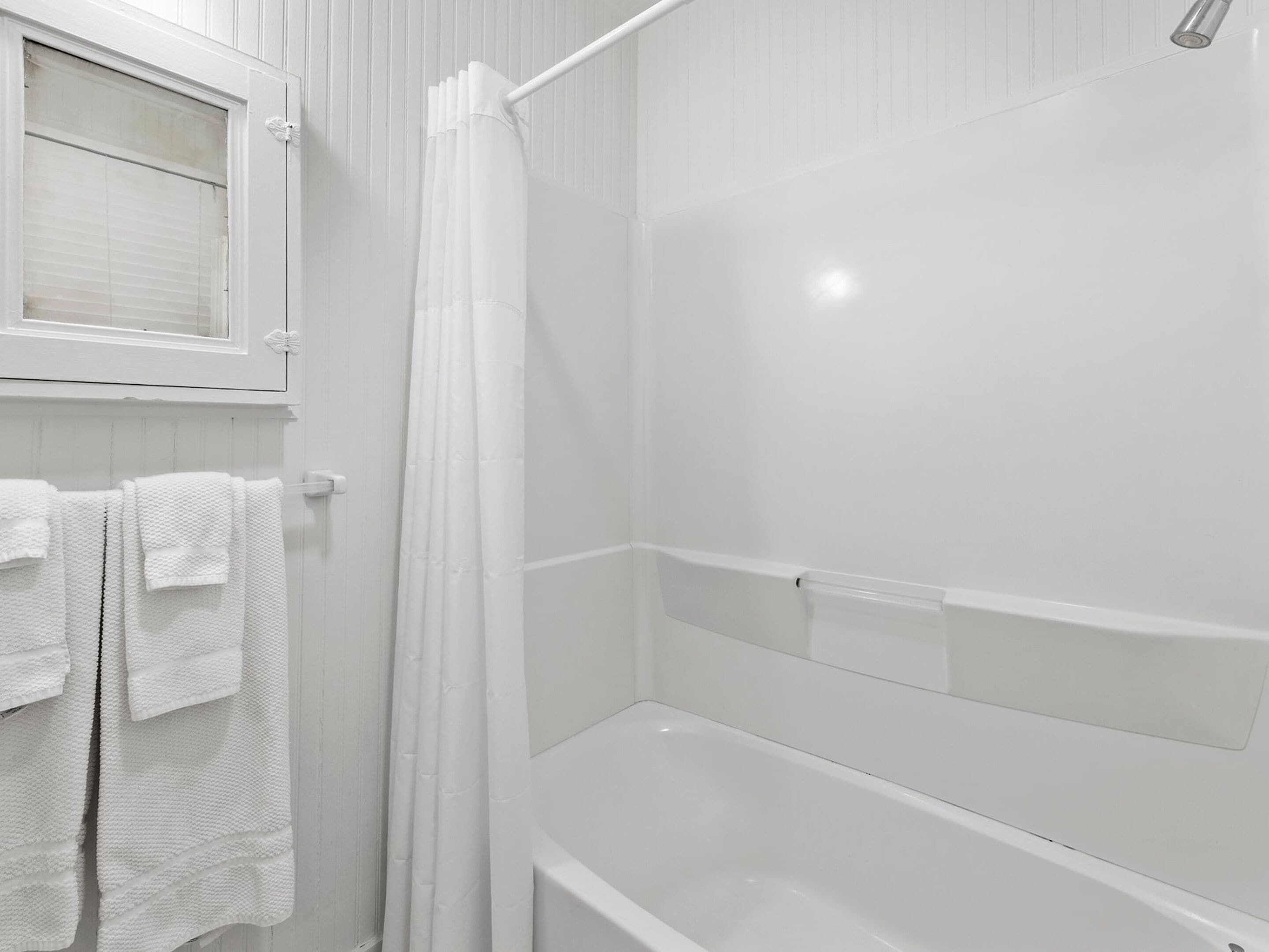 A white bathroom with a shower, a bathtub, and a window above the shower.