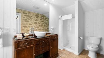 Une salle de bain avec un mur en pierre, un meuble-lavabo en bois, un lavabo blanc et des toilettes blanches.