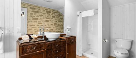 A bathroom with a stone wall, wooden vanity, white sink, and a white toilet.