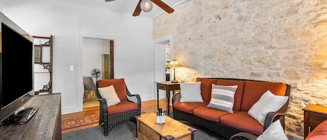 Un salón con pared de piedra, ventilador de techo, mobiliario de mimbre y una mesa de centro de madera.