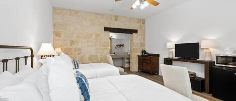 A hotel room with a large bed, a desk with a TV, a ceiling fan, and a stone accent wall.