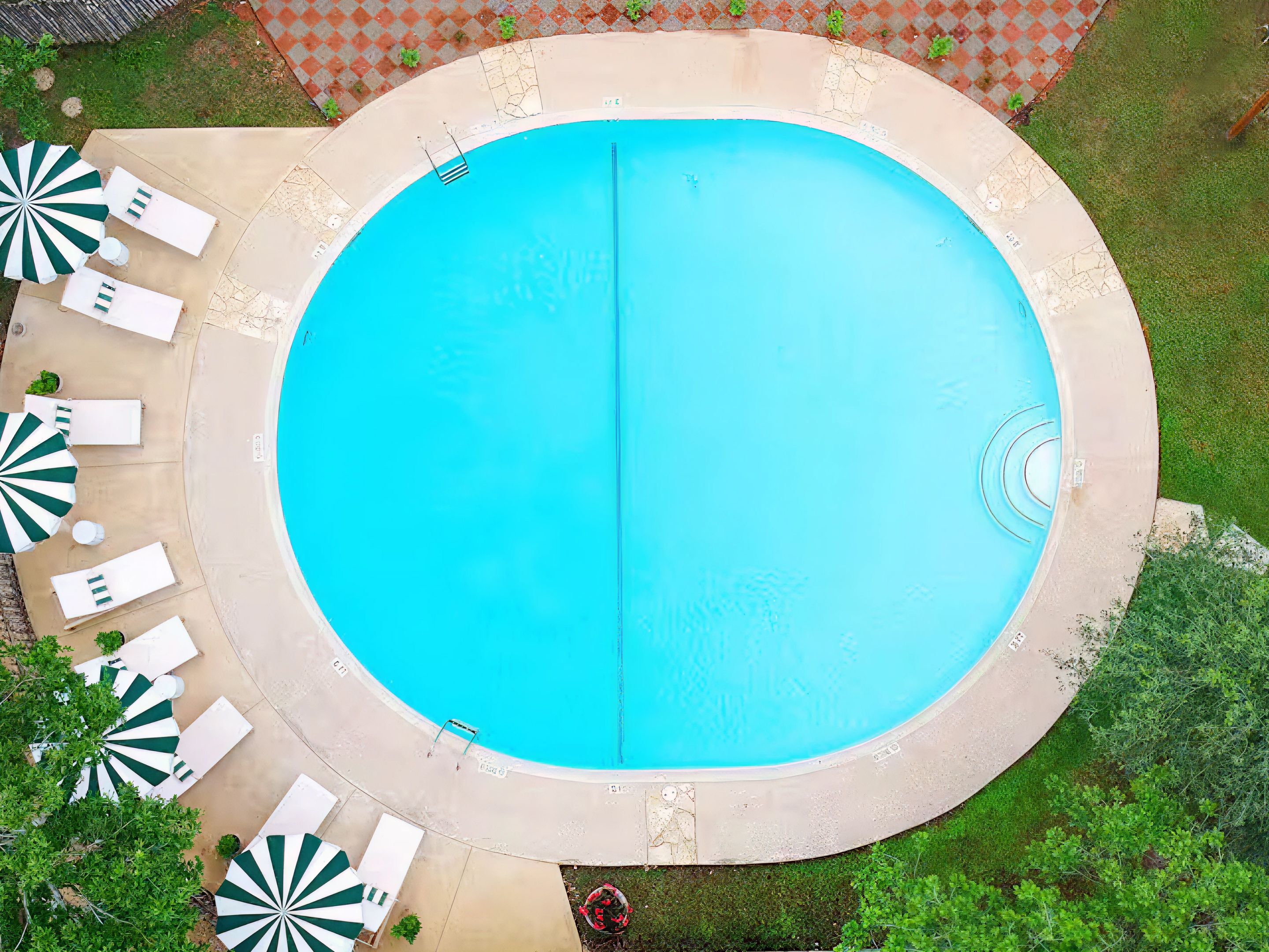 Ein kreisförmiger Swimmingpool mit einem klaren, blauen Beckeninneren, umgeben von einer Betonplattform. Mehrere Liegestühle und Sonnenschirme sind rund um den Pool angeordnet.
