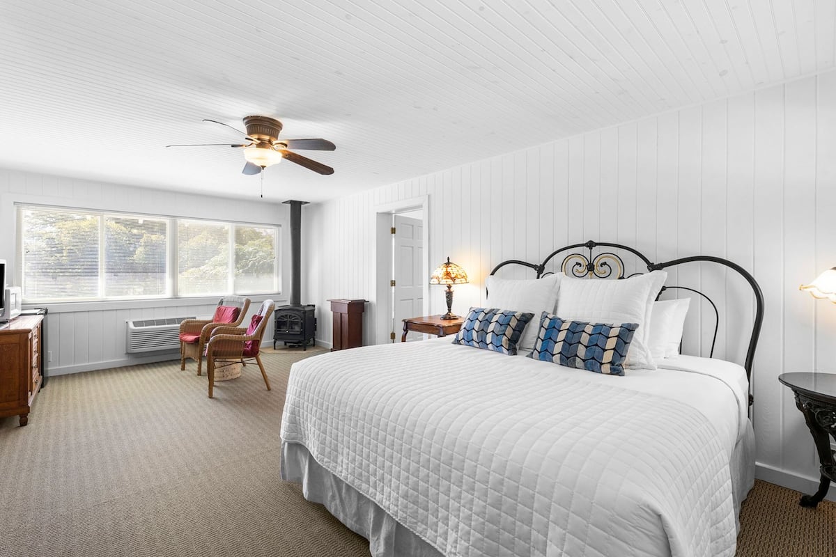 A bedroom with a large bed, a ceiling fan, a heater, a window with blinds, and a chair.