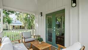 A covered porch with wooden furniture, a table, and a door with a green frame. - Meyer Hotel (Comfort)