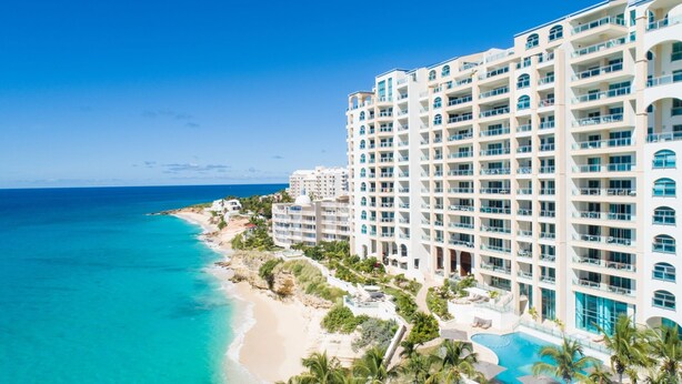 A beachfront hotel with multiple balconies, a swimming pool, and a beach view.
