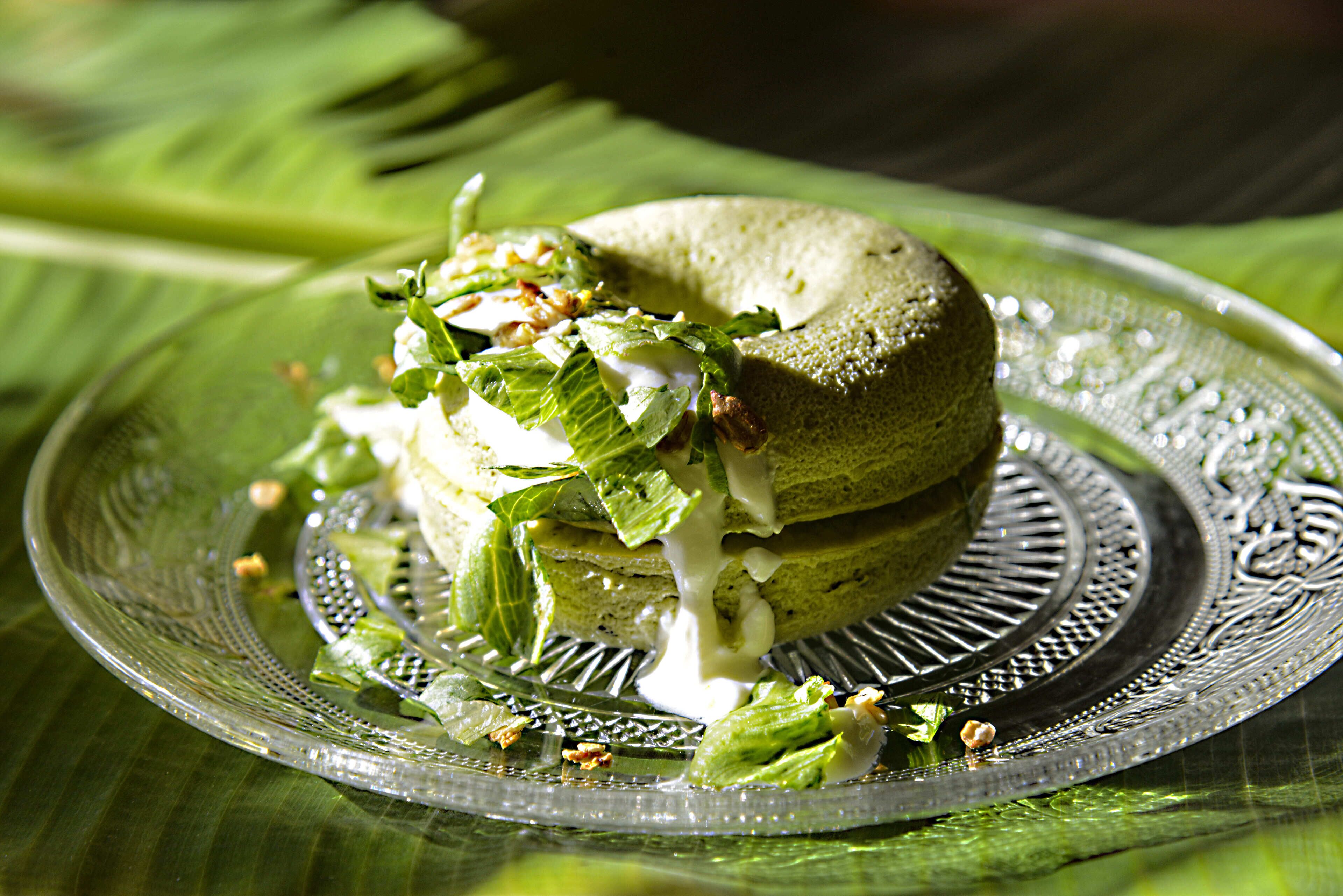 A sandwich on a decorative glass plate with a leaf pattern, placed on a green tablecloth.