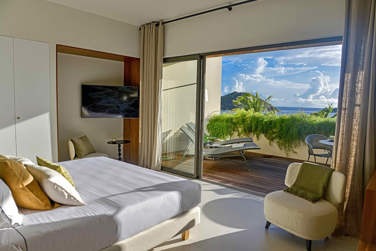 Una camera da letto moderna con un letto grande, vista sull'esterno e un balcone con posti a sedere.