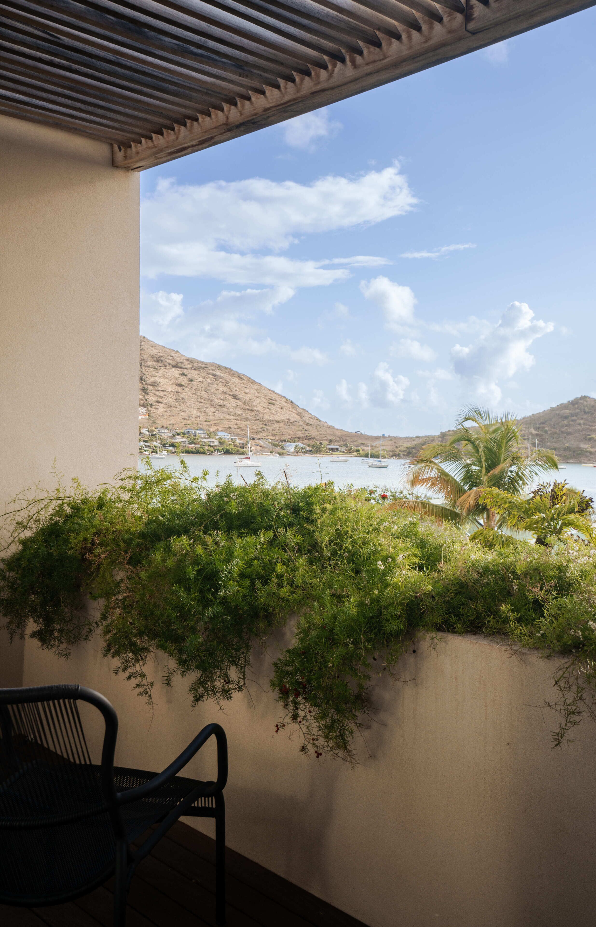 Un balcón con vista a un cuerpo de agua, una palmera y una silla.
