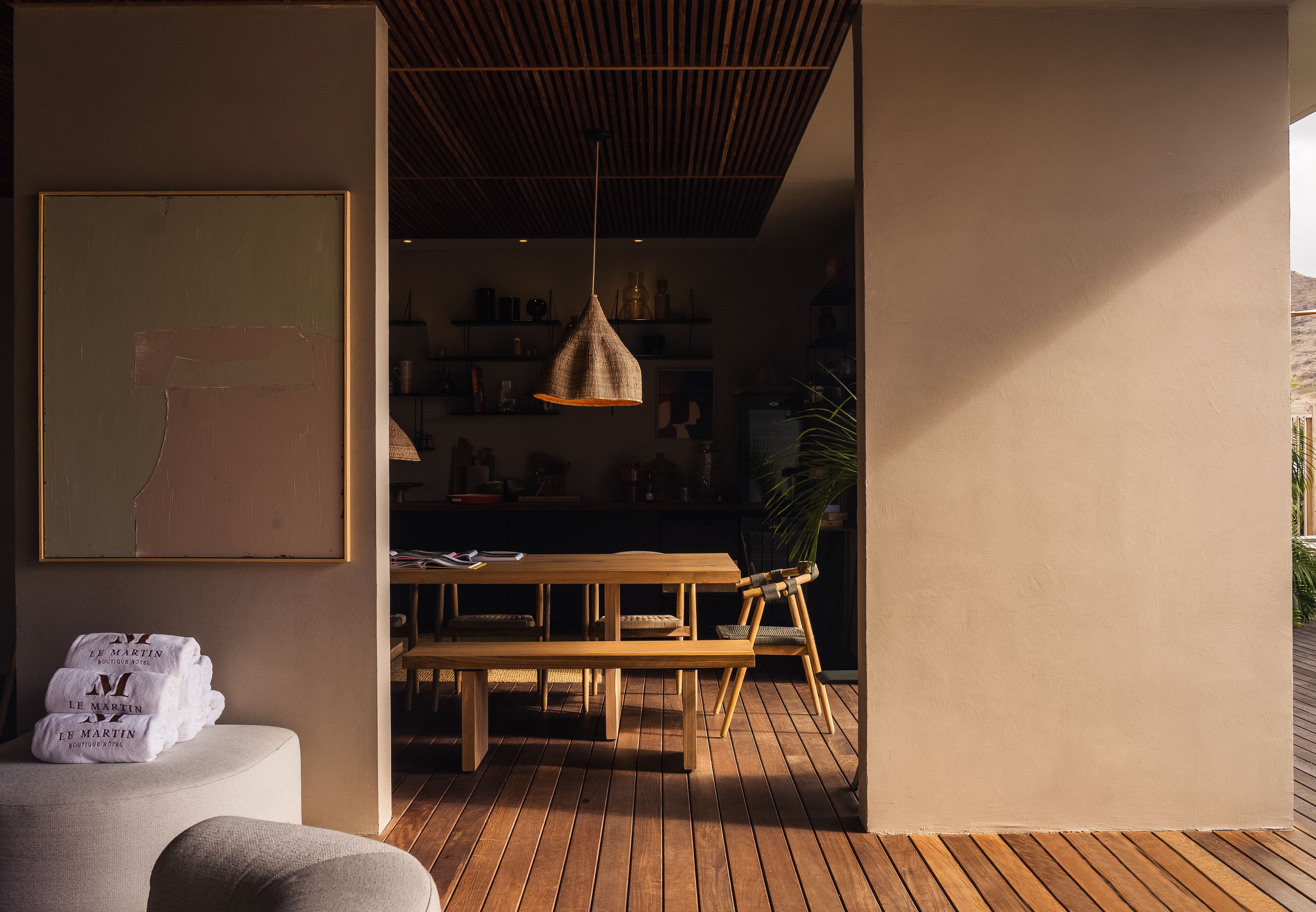 A wooden dining table with benches, a hanging light fixture, and a plant in a modern interior space.