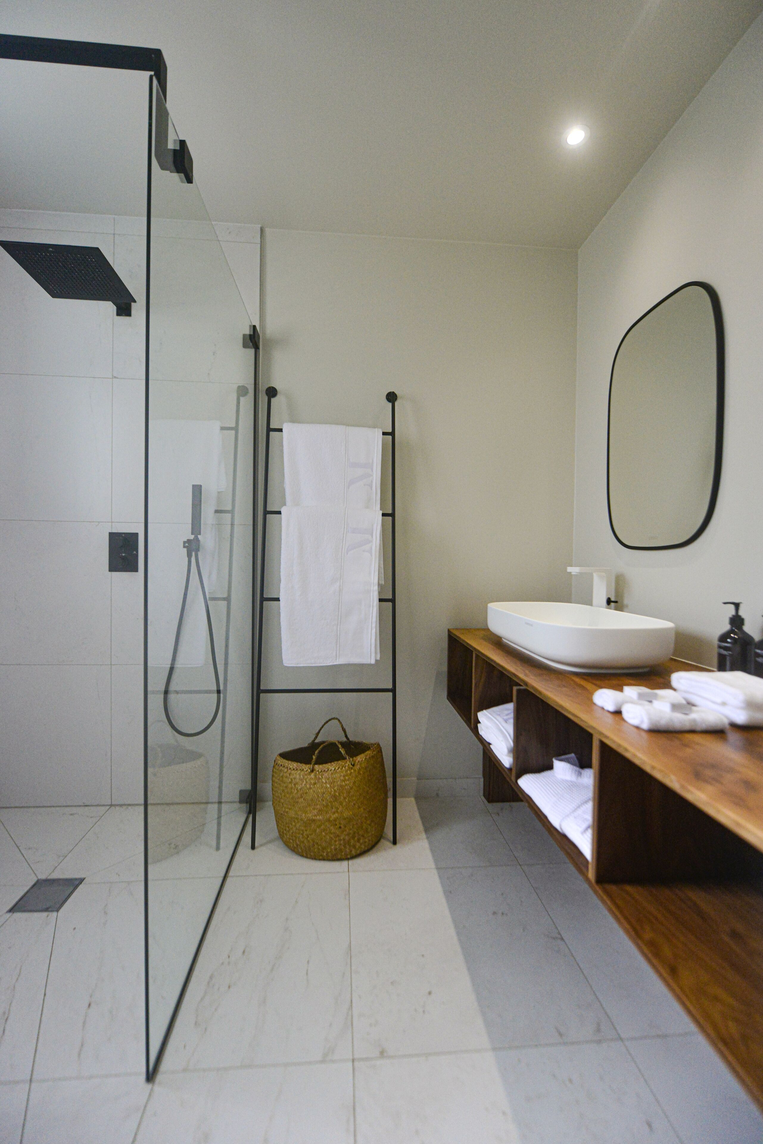Un bagno moderno con cabina doccia in vetro, mobile bagno in legno con lavandino e uno specchio grande.