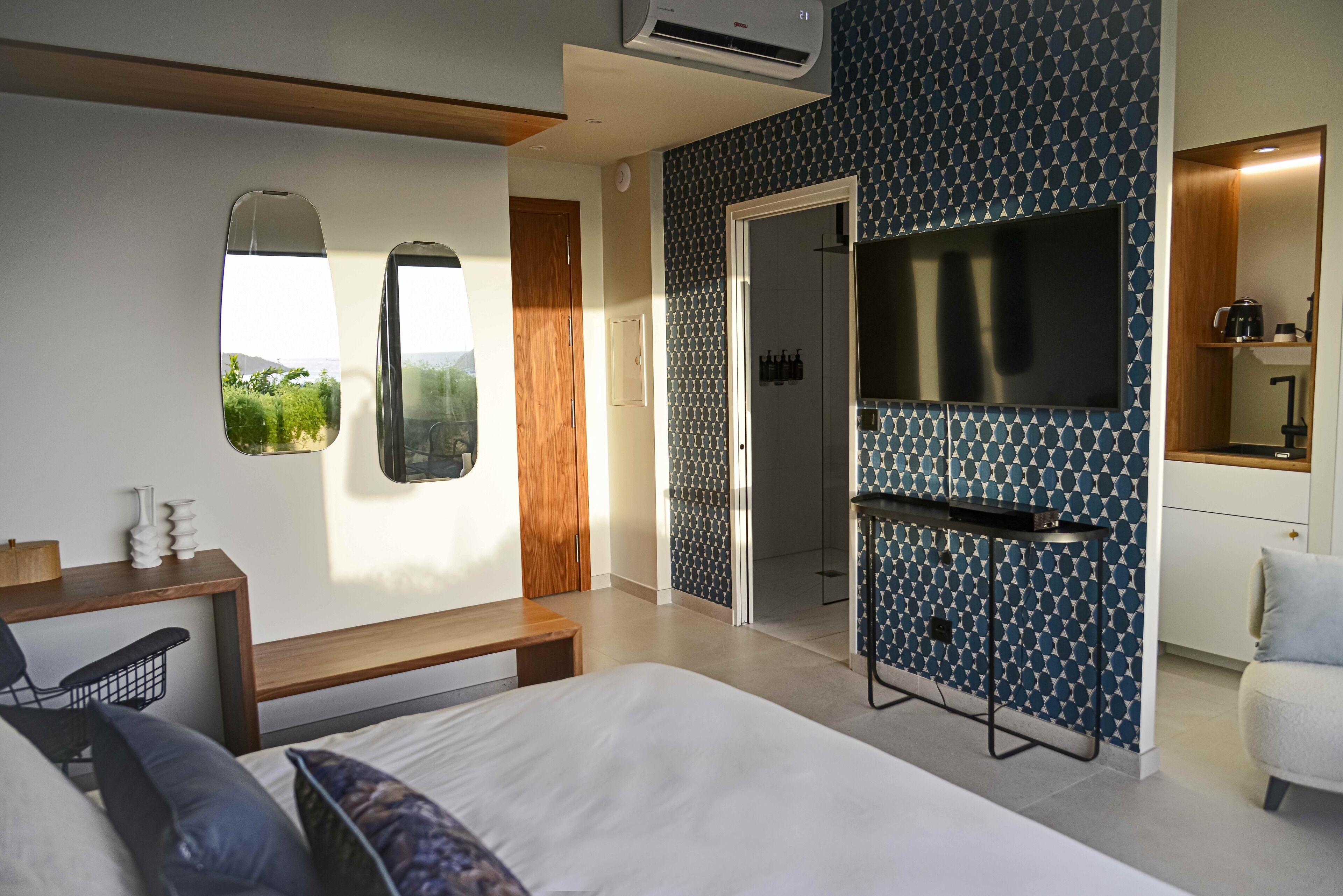 A modern hotel room with a large bed, a desk, a TV, and a bathroom visible through a door.