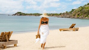 A beach with a woman walking, wooden lounge chairs, and a clear sky. - Le Martin Boutique Hôtel (Cul de Sac)