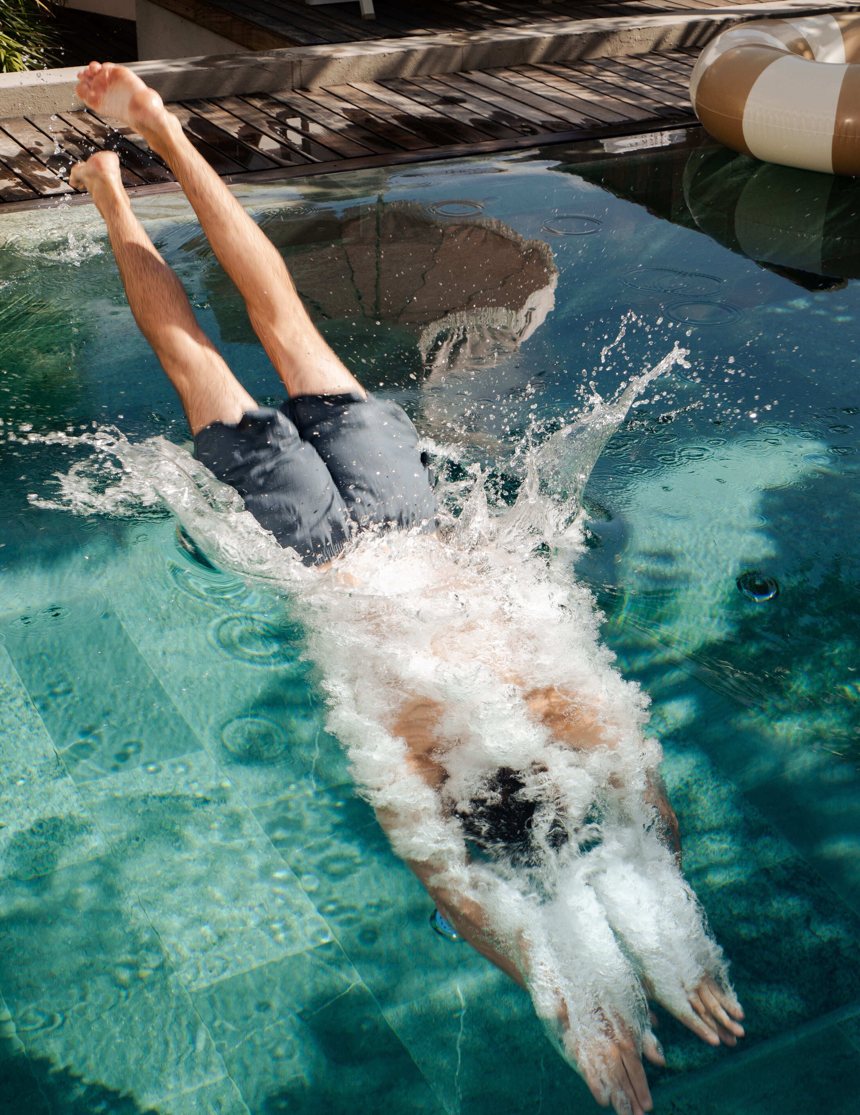 A person swimming in a pool with clear water and a wooden deck in the background.