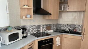 Eine kleine Küche mit Mikrowelle, Herd und Spüle. Sie verfügt über Holzschränke, eine geflieste Spritzschutzwand und eine kleine Arbeitsfläche.